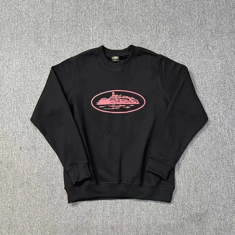 Black crewneck sweatshirt with a pink oval graphic laid flat on a grey surface