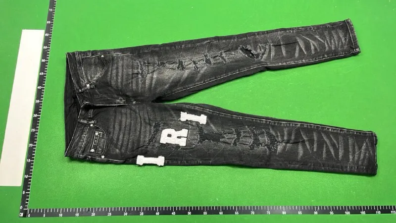 Dark distressed jeans laid diagonally on a green surface beside ruler markings